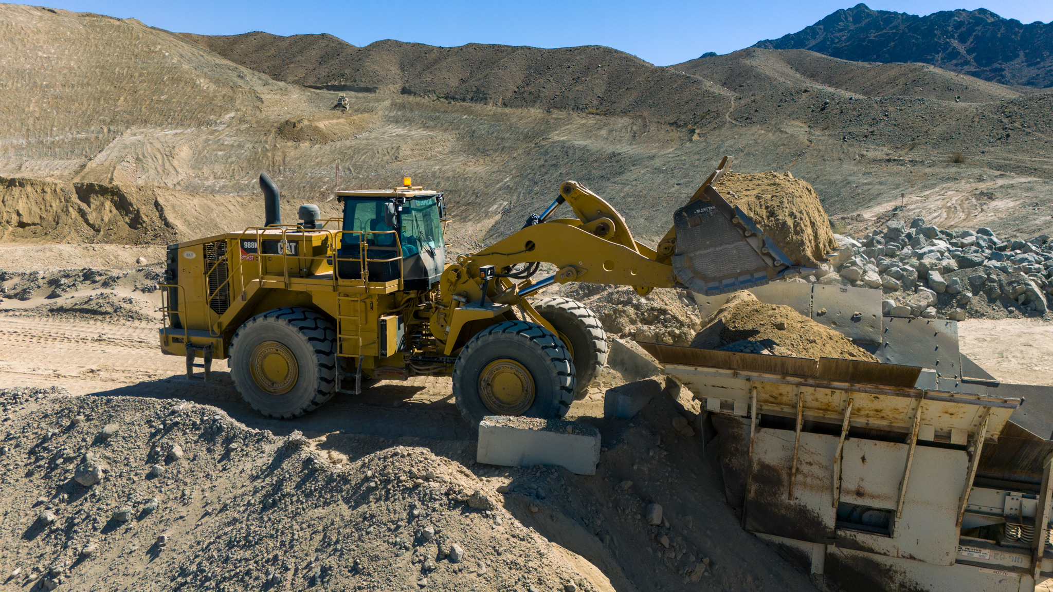 A yellow bulldozer moves dirt at a mining site, with rocky hills in the background under a clear blue sky. A yellow bulldozer moves dirt at a mining site, with rocky hills in the background under a clear blue sky.